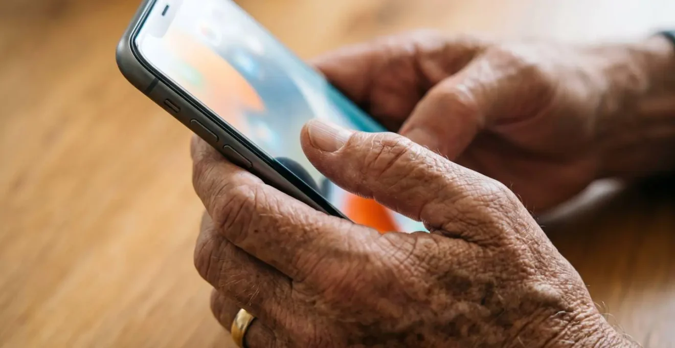 Mani anziane che tengono delicatamente uno smartphone con schermo luminoso e icone grandi